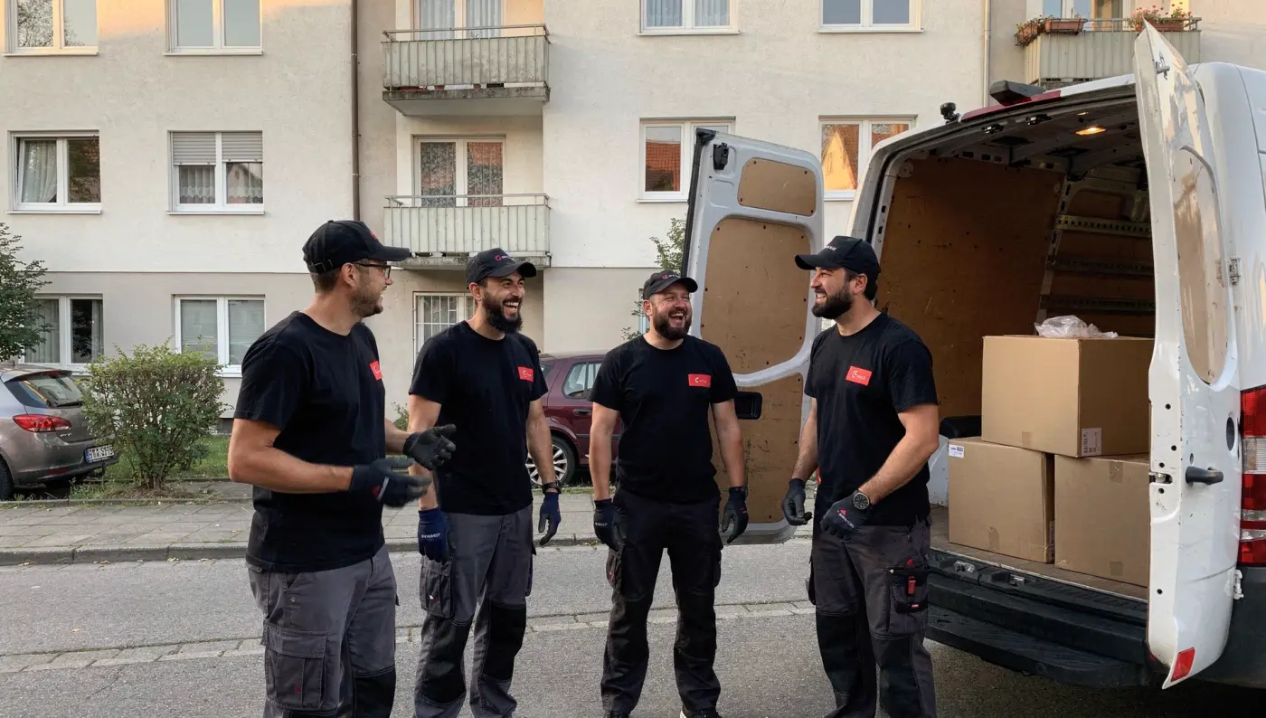Das Team der Rümpel Türken in schwarzen Shirts lacht vor dem offenen Transporter.